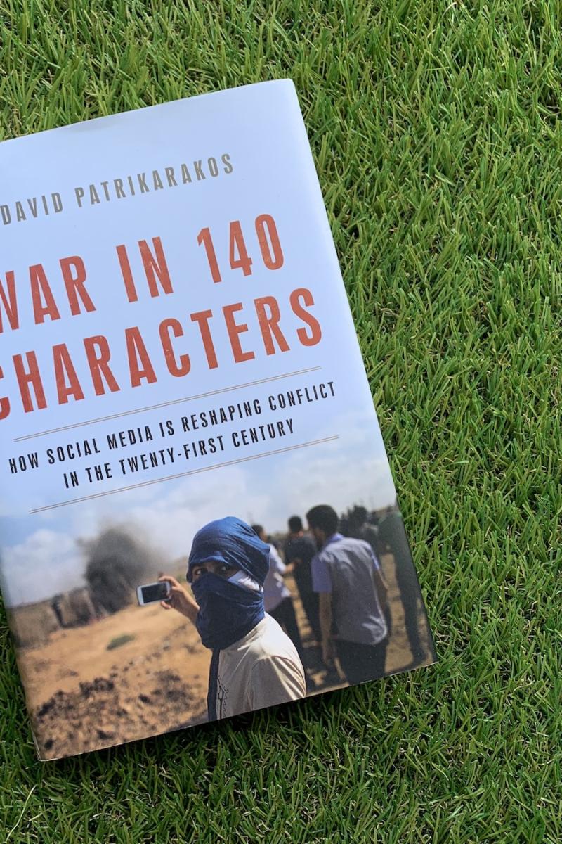A photo of the book "War in 140 characters" by David Patrikarakos is on top of a rug that looks like green grass.