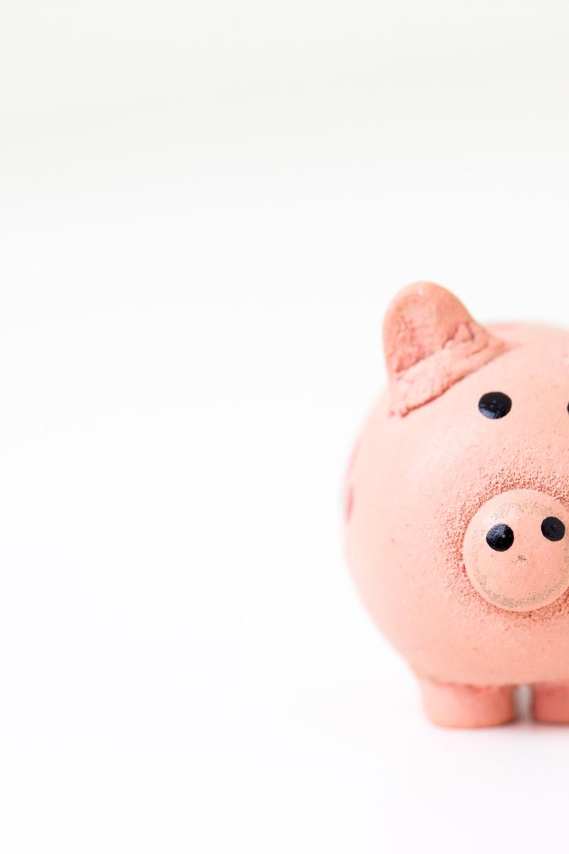 A pink piggy bank sits on a white surface on the right hand side of the image.