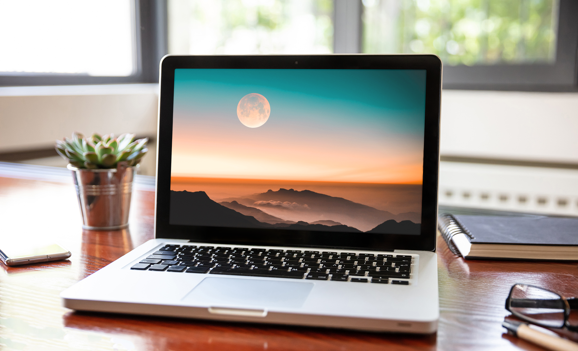 An open laptop sits on a table. To the right is a notebook.