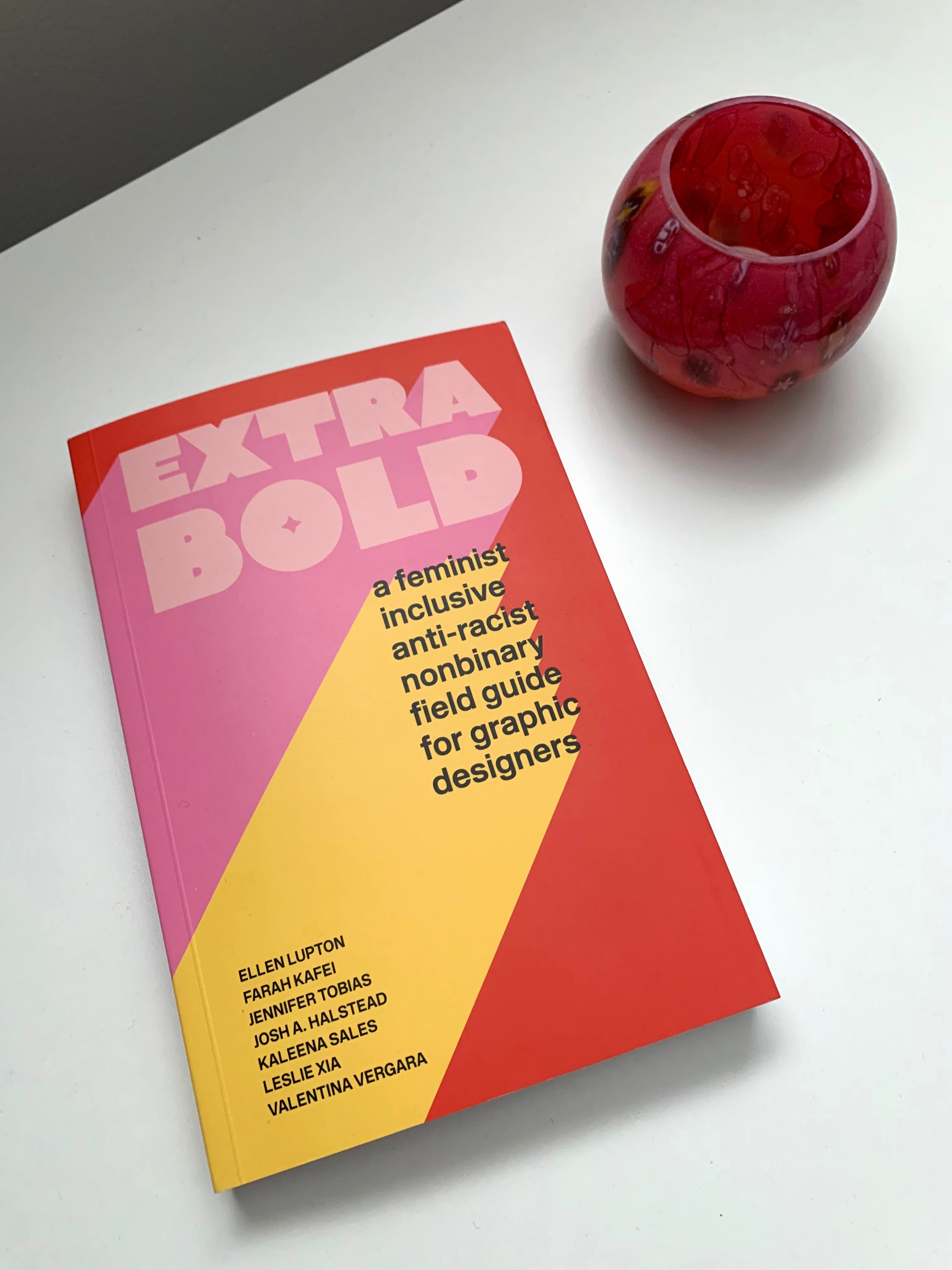The book "Extra Bold" sits on a white desktop to the left of a pink candle holder.