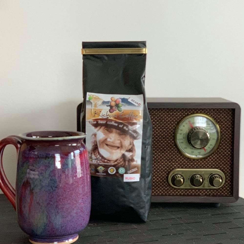 A purple mug and a bag of coffee sit in front of, and on the left, of a radio.