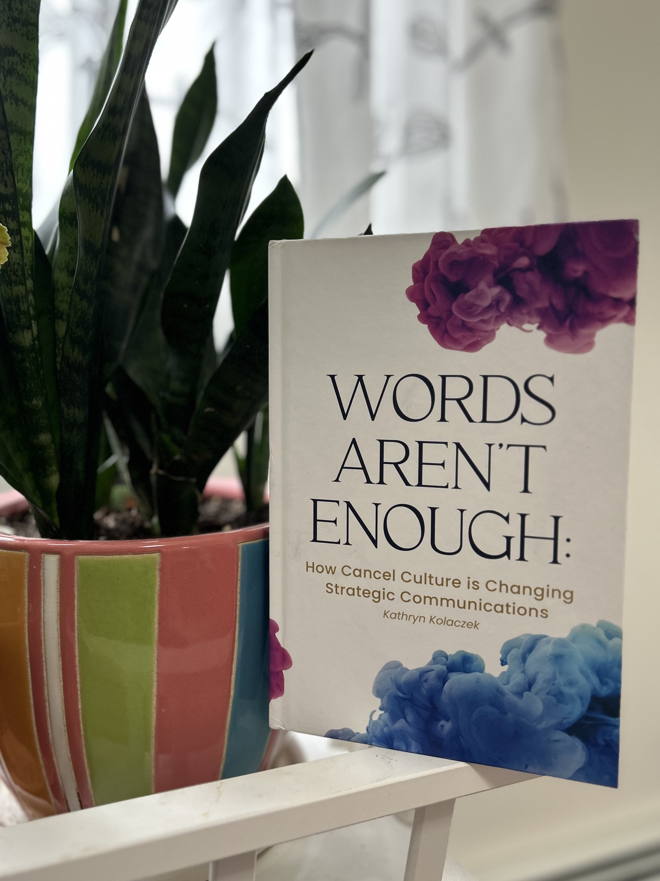 The book "Words Aren't Enough" is propped up beside a plant.