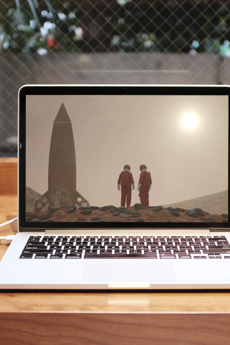 An open Macbook is on a table in a coffee shop. A coffee cup sits on the left. The screen is an image of two astronauts beside a rocket.